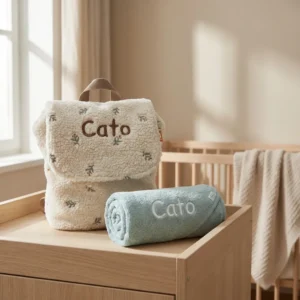 Gepersonaliseerde babyrugzak en handdoek met de naam Cato op houten commode in babykamer
