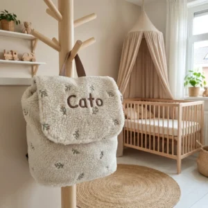 Teddy tas met naam Cato hangend aan houten kapstok in neutrale babykamer met ledikant en hemelbed