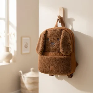 Bruine pluche kinderrugzak met hondengezicht hangend aan houten wandhaak in lichte kinderkamer