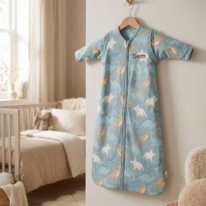 Blauwe babyslaapzak met dierenprint op houten hanger in lichte babykamer met ledikant