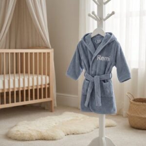 Blauwe kinderbadjas met naam Remi geborduurd, hangend aan kapstok in lichte babykamer met ledikant