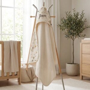 Houten standaard met beige badcape en handdoeken in lichte babykamer met ledikant en plantenpot